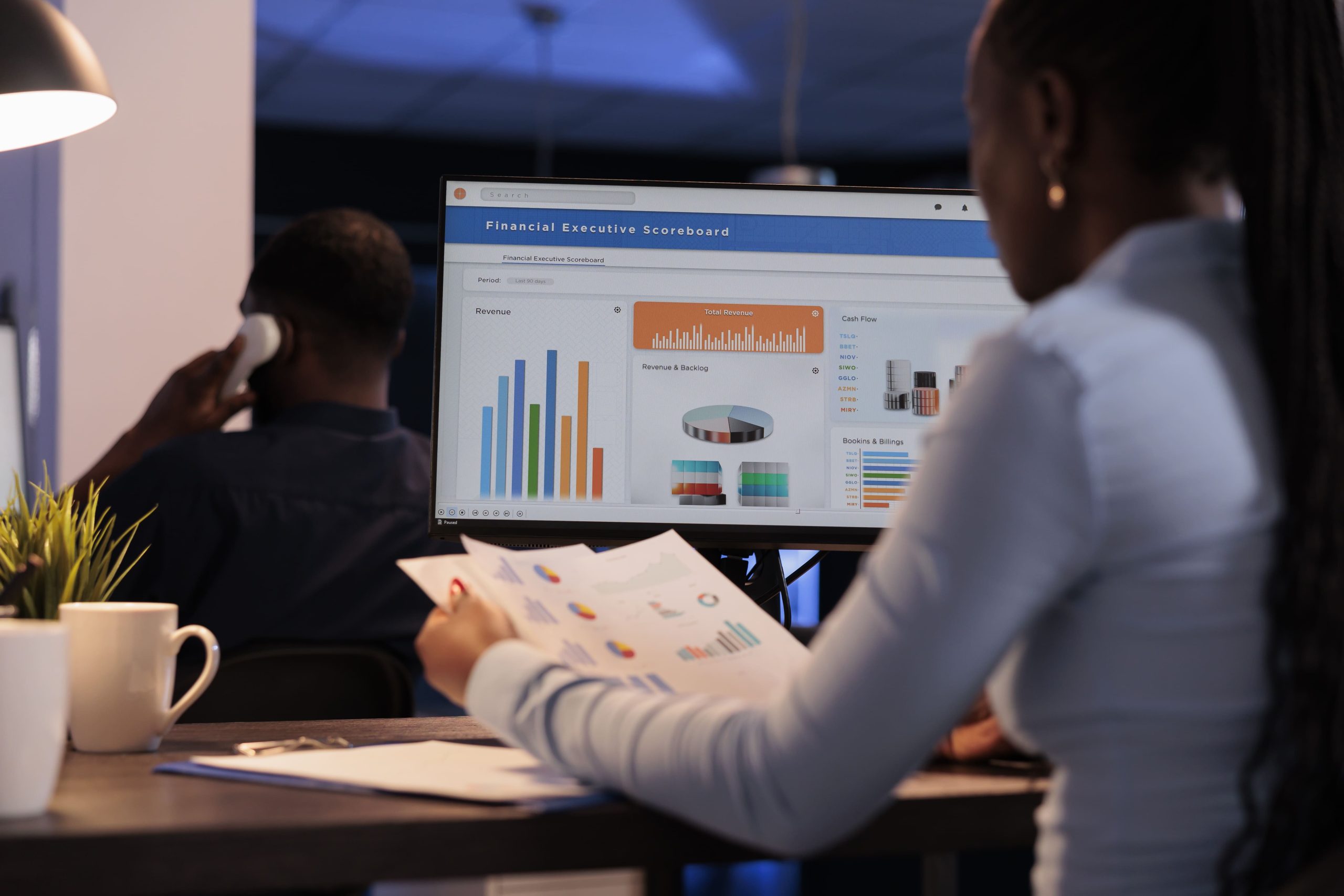 young businesswoman working with statistics charts computer monitor analyzing company data paperwork using online information create research report before deadline night after hours (1)
